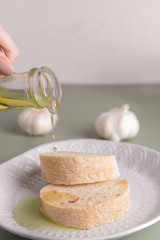 Woman pouring tasty olive oil from bottle onto fresh bread