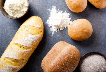 Top view of different kinds of bread, bowls with flour on grey rustic surface.Concept of varius of bakery products