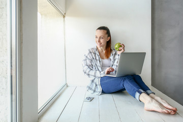 Young woman eating apple while working on laptop indoors