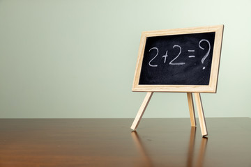 Blackboard with easel stand on wooden table. Written an elementary maths calcul on the blackboard...