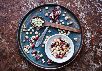 Dry beans, chickpeas, green peas in a plate and in spoons vegan food top view space for text
