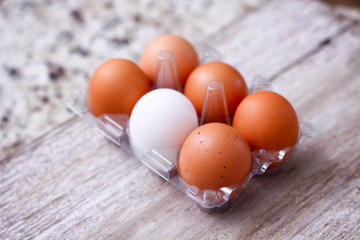 Set of brown and white eggs in clear plastic box on wooden table.