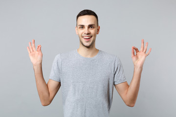 Fototapeta premium Portrait of smiling young man in casual clothes holding hands in yoga gesture relaxing meditating isolated on grey background in studio. People sincere emotions, lifestyle concept. Mock up copy space.