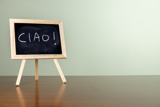 Blackboard with easel stand on wooden table. Written "ciao" on the blackboard With copy space. education concept.