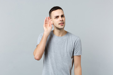 Portrait of curious young man in casual clothes looking camera hearing holding hand near ear...
