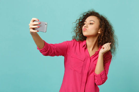 Cute african girl in casual clothes blowing sending air kiss, doing selfie shot on mobile phone isolated on blue turquoise background. People sincere emotions, lifestyle concept. Mock up copy space.