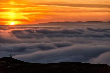 Silhouette of a man on the ridge above the sea of clouds, misty mountains at sunset in Iceland