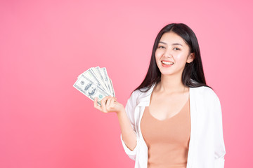 Successful beautiful Asian business young woman holding money US dollar bills in hand on pink background , business concept