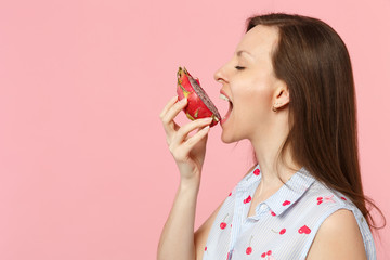 Side view of young woman in summer clothes biting half of fresh ripe pitahaya, dragon fruit isolated on pink pastel wall background. People vivid lifestyle relax vacation concept. Mock up copy space.