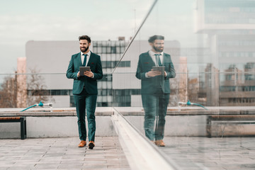 Young bearded successful businessman in formal wear walking on roof and holding tablet. Sometimes...