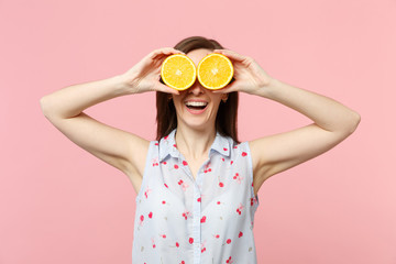 Smiling young woman in summer clothes holding covering eyes with halfs of fresh ripe orange fruit isolated on pink pastel background. People vivid lifestyle relax vacation concept. Mock up copy space.