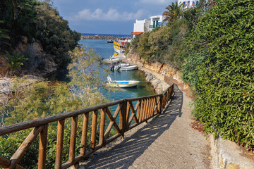 stone footpath with wooden railing steeply descending into the bay with boats in the Greek town of...