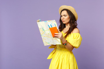Puzzled young woman in yellow dress, summer hat hold city map, passport boarding pass ticket isolated on pastel violet wall background. People sincere emotions, lifestyle concept. Mock up copy space.