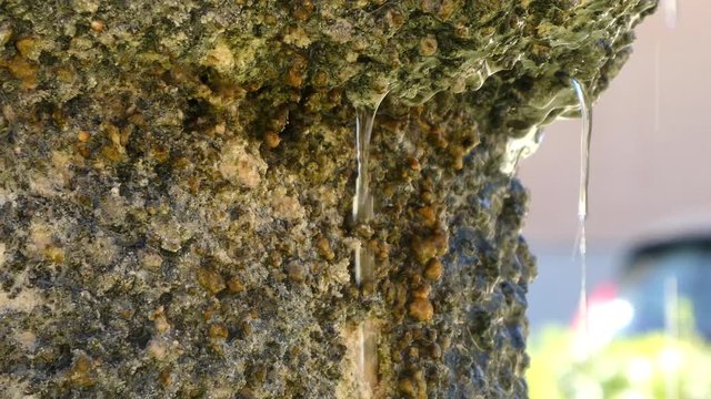 Close up detail of one side of an ancient stone fountain and water falling