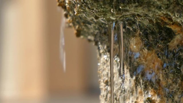 Close up detail of one side of an ancient stone fountain and water falling