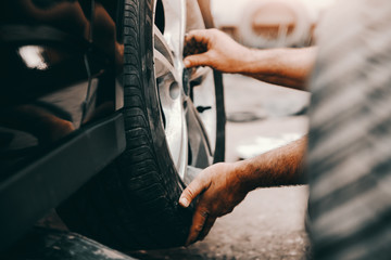 Close up of auto mechanic changing tire while crouching at workshop. Selective focus on hands.