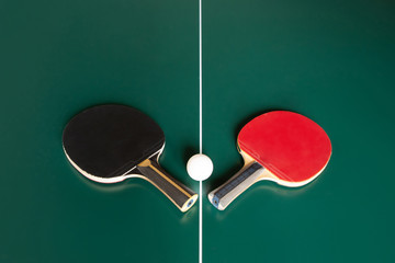 two ping-pong rackets and a ball on a green table. - obrazy, fototapety, plakaty