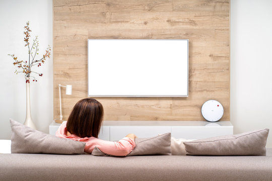Back view of beautiful young woman resting in luxury appartments, sitting on the sofa and watching TV.