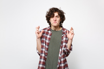 Displeased young man in casual clothes waiting for special moment, keeping fingers crossed making wish isolated on white wall background. People sincere emotions lifestyle concept. Mock up copy space.