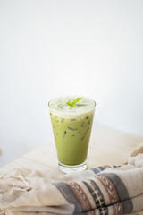 Ice green tea or matcha latte on white wood table and clothes decoration object.