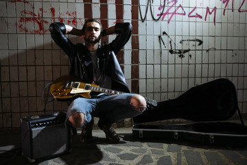 Street musician sitting and holding a guitar in the underpass. Vagrant lifestyle. Playing in the underpass to make a living. Unemployed musician. Future rock star.