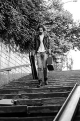 Street musician holding a case with a guitar and amplifier. Goes down the stairs to the underground passage. Vagrant lifestyle. Playing to make money a living. Unemployed musician. Future rock star.