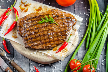 grilled kebab grilled meat steak lies on a wooden vintage old board rustic, chili, with tomatoes,...