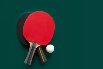 Two ping-pong rackets and a ball on a green table.