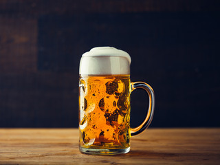 Glass of fresh beer with foam on wooden table