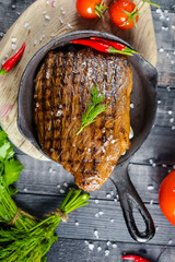 grilled kebab grilled meat steak lies in an iron frying pan, on a wooden vintage old board rustic,...