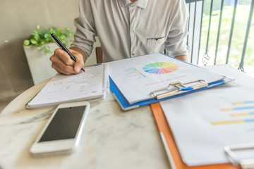 Young man reading financial data on document and writing notes