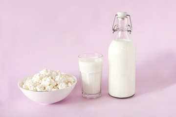 Fresh cottage cheese and milk for breakfast in a glass bottle and a glass of milk in the center of the frame on a pink background