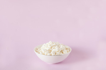Fresh cottage cheese for breakfast in a white bowl in the center of the frame on a pink background