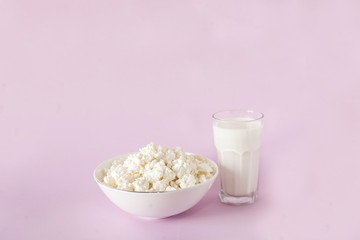 Fresh cottage cheese for breakfast in a white bowl and glass of milk in the center of the frame on a pink background