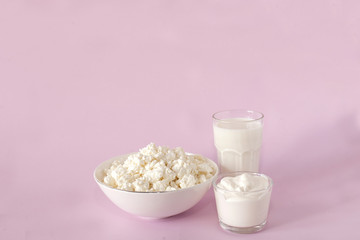Fresh cottage cheese for breakfast in a white bowl, sour cream and glass of milk in the center of the frame on a pink background