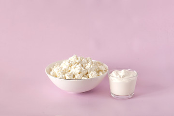 Fresh cottage cheese for breakfast in a white bowl, sour cream in the center of the frame on a pink background