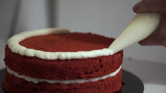 Making red velvet cake at home. Smearing a layer of cake cream around the circumference. Close up