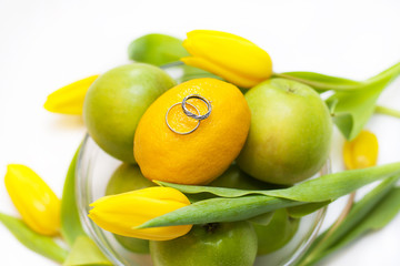 Wedding rings lie on lemon and aplles with yellow tulips