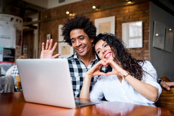 Multiethnic latin couple sitting together at cafe and video chatting using laptop