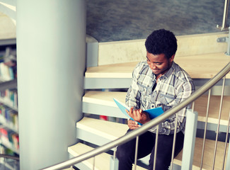 education, high school, university, learning and people concept - happy african american student boy or young man reading book sitting on stairs at library