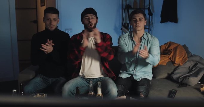 Three men listening the Hymn before watching a football match on the TV at home. The fans cheering best soccer team.