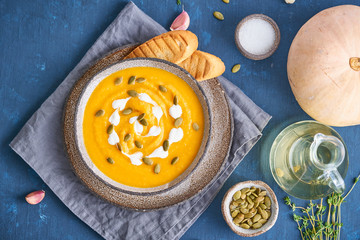 Pupmkin cream soup puree on dark bright blue wooden table, dietary vegetarian lunch, top view, close up.