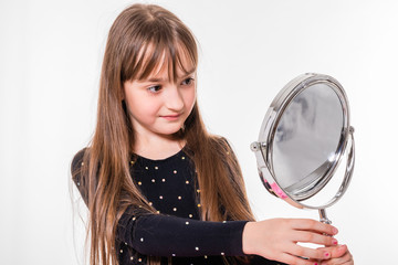 A smiling girl of about nine with long hair attentively examines herself in the mirror