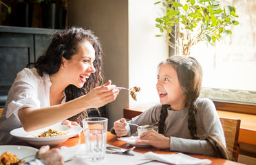 Latin mom and daughter eating together lunch at restaurant, multiethnic family having fun