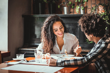 Happy young couple eating lunch together at restaurant, african american people having fun