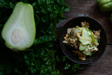 Fresh chayote fruits (Sechium edulis) stir fried with egg and garlic in bowl on wood background