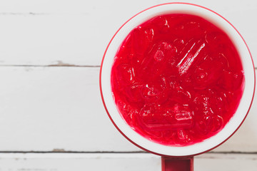 Top view of red cold drink in cooler flask on white wooden.