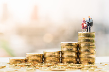 Concepts of retirement planning and finanacial. Miniature people: Old couple figure standing on top of coin stack.