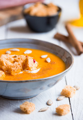 Delicious pumpkin soup in a bowl with croutons on white wood