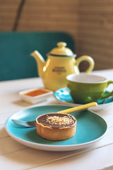 Salted caramel round cake on blue plate with fork, yellow tea pot and green cup. Delicious caramel chocolate tart, topped with nuts